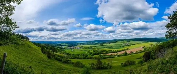 Panoramablick auf grüne Wiesen und Hügel unter einem bewölkten Himmel